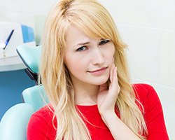 Woman in dental chair holding jaw