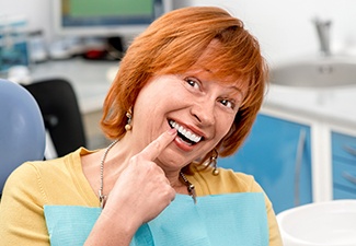 Older woman in dental chair pointing to smile