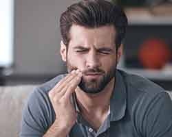 Bearded man rubbing his jaw in pain