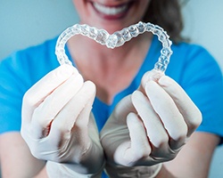 Dentist in blue scrubs and white gloves holding clear aligners in a heart shape