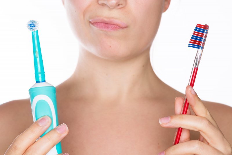 Woman holding an electric and manual toothbrush