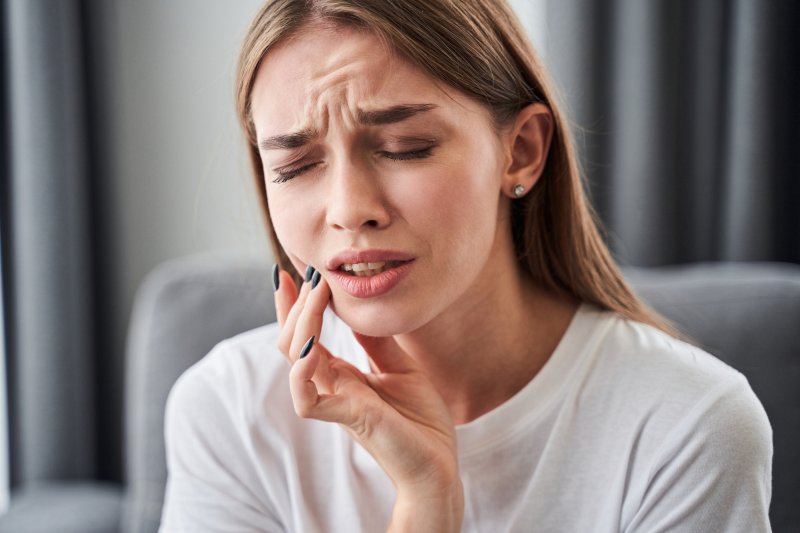 Young woman with right hand on her cheek and furrowed brows experiencing a toothache