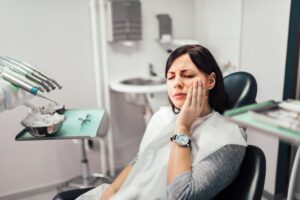 Woman clutching jaw in pain in the dentist's chair. 